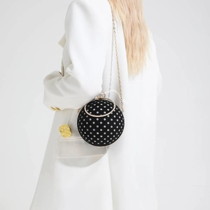 Polka dot sphere clutch bag with gold ring handle worn by model in white suit