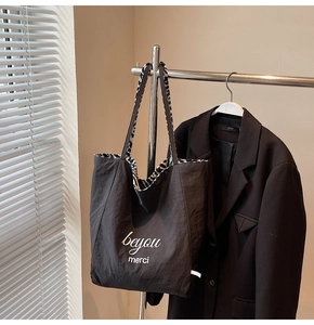 Detail of black tote bag featuring white Merci lettering and striped inner lining
