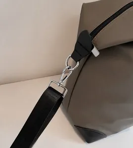 Dettaglio del gancio girevole in metallo argento e cinturino nero sulla borsa da viaggio grigia