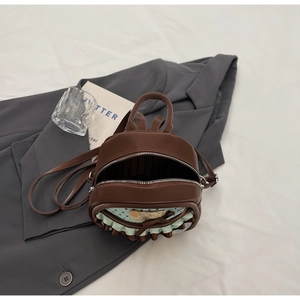 Detail of a brown mini backpack with bow and cartoon patch showing dual zipper and interior