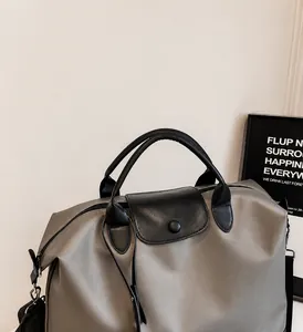 Dettaglio della borsa da viaggio in nylon grigio con manici in pelle nera e patta a scatto