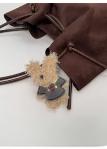 Close-up of a plush rabbit charm in a grey sweater on a brown suede tote bag