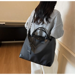 Dettaglio della borsa da viaggio in nylon nero con manici in pelle e charm NOCO