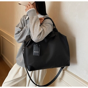 Dettaglio di borsa da viaggio in nylon nero con manici in pelle e targhetta NOCO