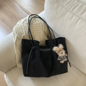 Detail of black suede tote bag with cute teddy bear charm on cozy beige knit background
