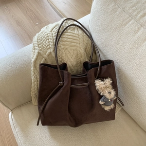 Detail of dark brown suede tote bag with drawstring texture and cute plush bear charm
