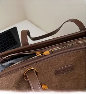 Detail of smooth bronze zipper and leather brand tag on brown suede tote bag