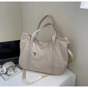 Detail van een grote beige nylon draagtas met functionele ritsen op een wit bureau