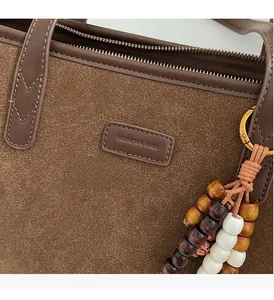 Detail of coffee suede tote bag with leather trim and wooden bead keychain accessory