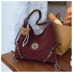 Detail of wine red leopard hobo bag with M logo, chain, and cute brown plush bear charm