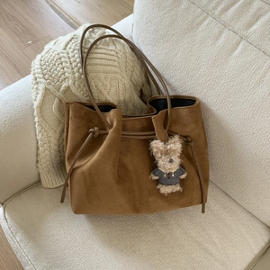 Close-up of brown suede tote bag with drawstring closure and cute plush bear charm accessory