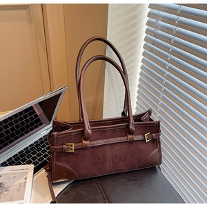 Detail of dark brown suede and leather stitching bag with gold buckle on office desk