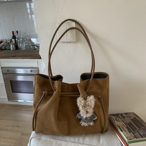 Detail of brown suede tote bag with drawstring side and cute bear plush pendant charm