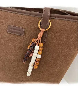 Detail of a matte brown tote bag with ethnic wooden bead charm and embossed logo tag