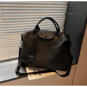Dettaglio di una grande borsa da viaggio in nylon nero con manici in pelle sul davanzale