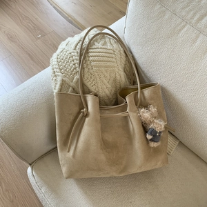Detail of khaki suede tote bag with delicate shoulder straps and a cute teddy bear charm