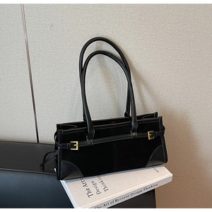 Detail of minimalist black suede shoulder bag with gold hardware and leather trim accents