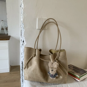 Detail of khaki suede tote bag featuring slim straps and a cute plush puppy pendant