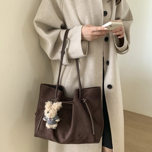 Detail view of brown suede tote bag featuring a cute teddy bear plush charm accessory