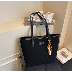 Detail view of black suede tote bag with leather straps and decorative bead tassel pendant