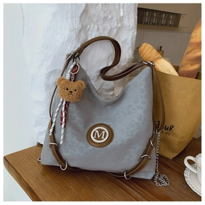 Detail of grey patterned hobo bag with brown leather trim and plush bear charm accent