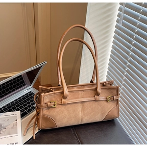Detailed view of caramel leather tote bag with suede texture and metal buckle on office desk