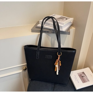 Detail of black matte tote bag with wooden bead charm and metal logo on white shelf