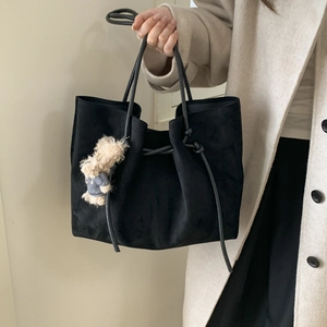 Detailed texture of black suede tote bag with a cute plush bear charm accessory