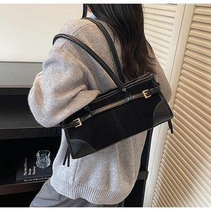 Detail view of black faux suede underarm bag with gold buckles on a female model
