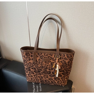 Detail of leopard print tote bag featuring wooden bead tassel and brown leather handle