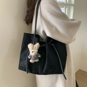 Detail view of black faux suede tote bag with slim straps and a cute plush bear charm