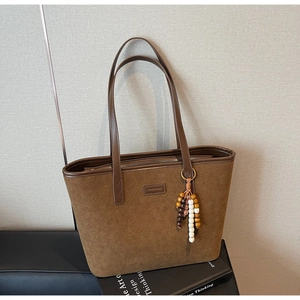 Detail of brown suede tote bag with leather strap and decorative beaded tassel charm