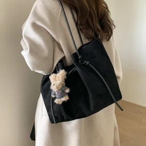 Detail of a black suede tote bag featuring a cute teddy bear charm on white wool coat