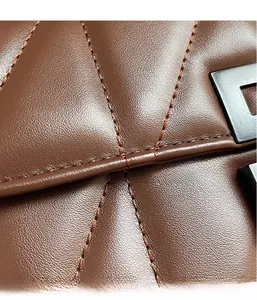 Detail shot of brown quilted leather texture and dark gray metal lock on the shoulder bag