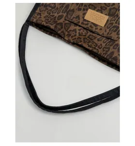 Detail of leopard print canvas tote bag featuring leather label and woven handles