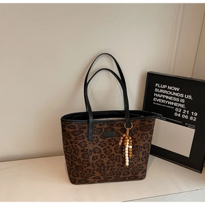 Detail of leopard print tote bag with black leather straps and wooden bead charm