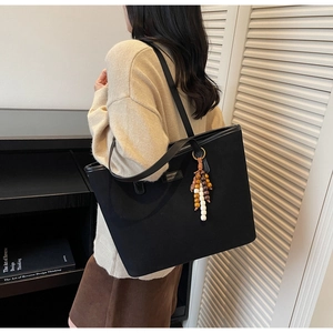 Detail of black tote bag with tassel charm and logo patch shown on shoulder
