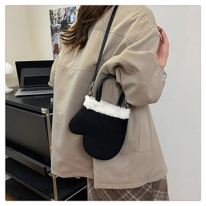 Detail shot of a black mitten-shaped crossbody bag with white sherpa trim on a model
