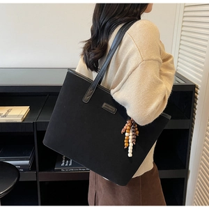 Detail of a large black matte tote bag featuring wooden bead charms and leather straps