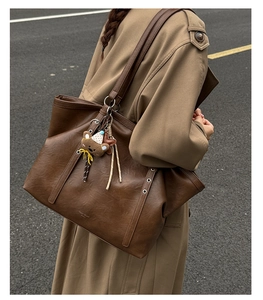 Close-up of textured dark brown leather tote bag with a cute plush bear charm detail