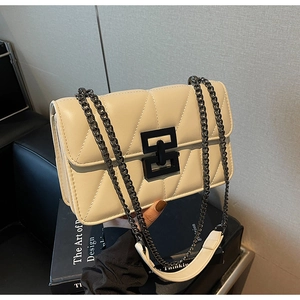 Close-up of beige quilted crossbody bag with black geometric metal lock and chain strap