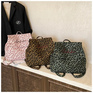 Three leopard print backpacks in pink, brown, and green on a wooden shelf with embroidery