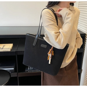 Detail of black tote bag with beaded charm accessory and minimalist branding tag