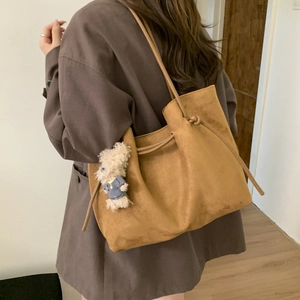 Detail of brown suede tote bag featuring a decorative side knot and plush bear charm
