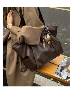 Detail of chocolate brown leather tote bag with silver eyelets and plush bear charm