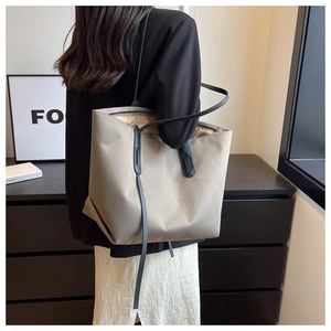 Détail d'un grand sac cabas en nylon taupe avec lanières en cuir noir porté par un modèle