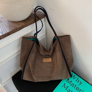 Detail of brown suede tote bag with black handles and green checkered inner lining
