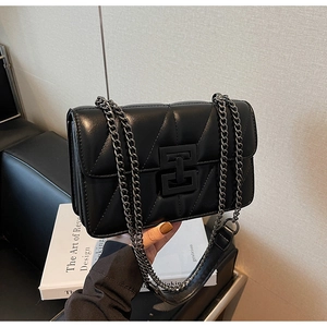Detail of black quilted crossbody bag with V-shaped stitching and dark metal chain