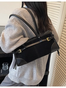 Elegant black suede and leather shoulder bag with gold buckles for women in a home setting