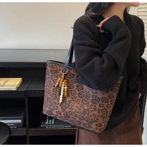 Detail of leopard print tote bag featuring wooden bead tassel and metal logo plate